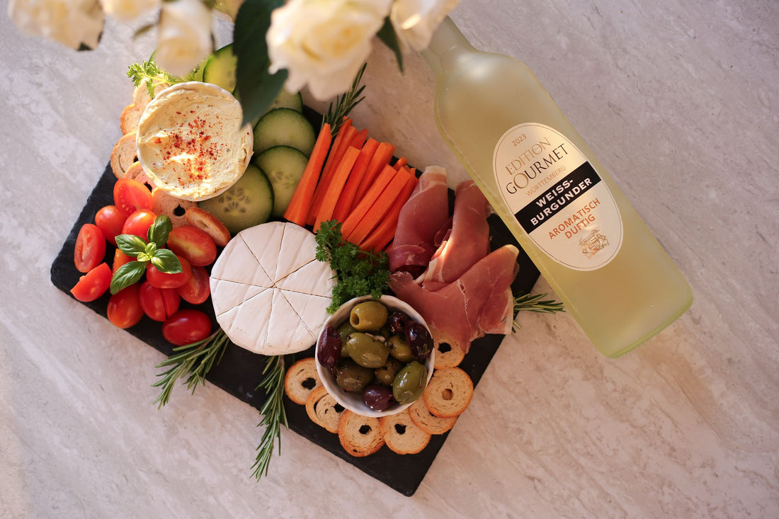 WZG Edition Gourmet Weißer Burgunder neben einer Antipasti-Platte mit Käse, Schinken und Oliven