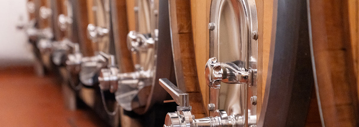 Edelstahltanks und Holzfässer in der Weinproduktion der WZG mit sichtbaren Armaturen und Auslässen.