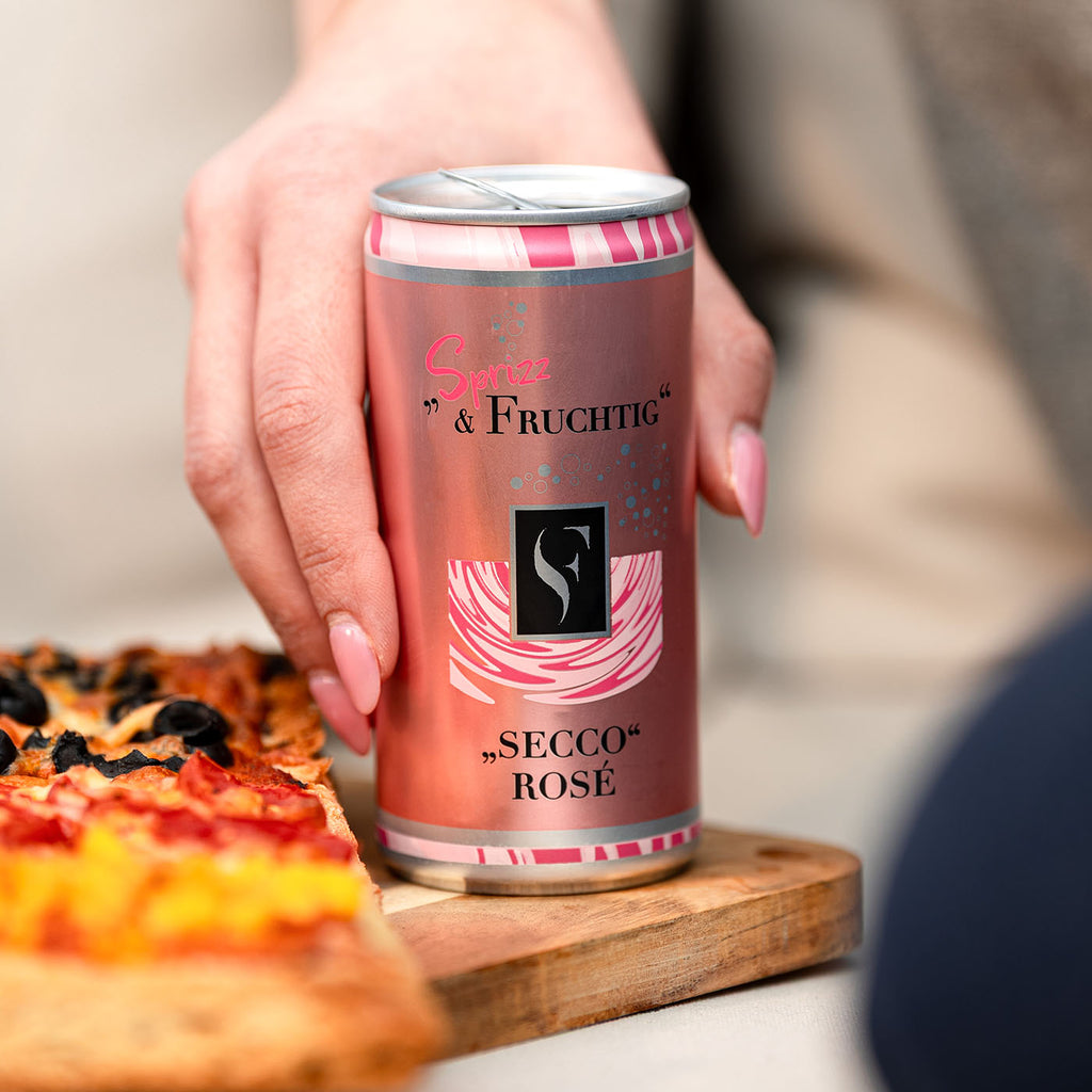 Sprizz & Fruchtig Secco Dose der WZG neben Pizza auf einem Holztisch.