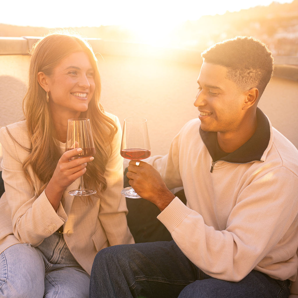 Frau und Mann stoßen bei Sonnenuntergang mit Süss & Fruchtig Rotwein der WZG an.