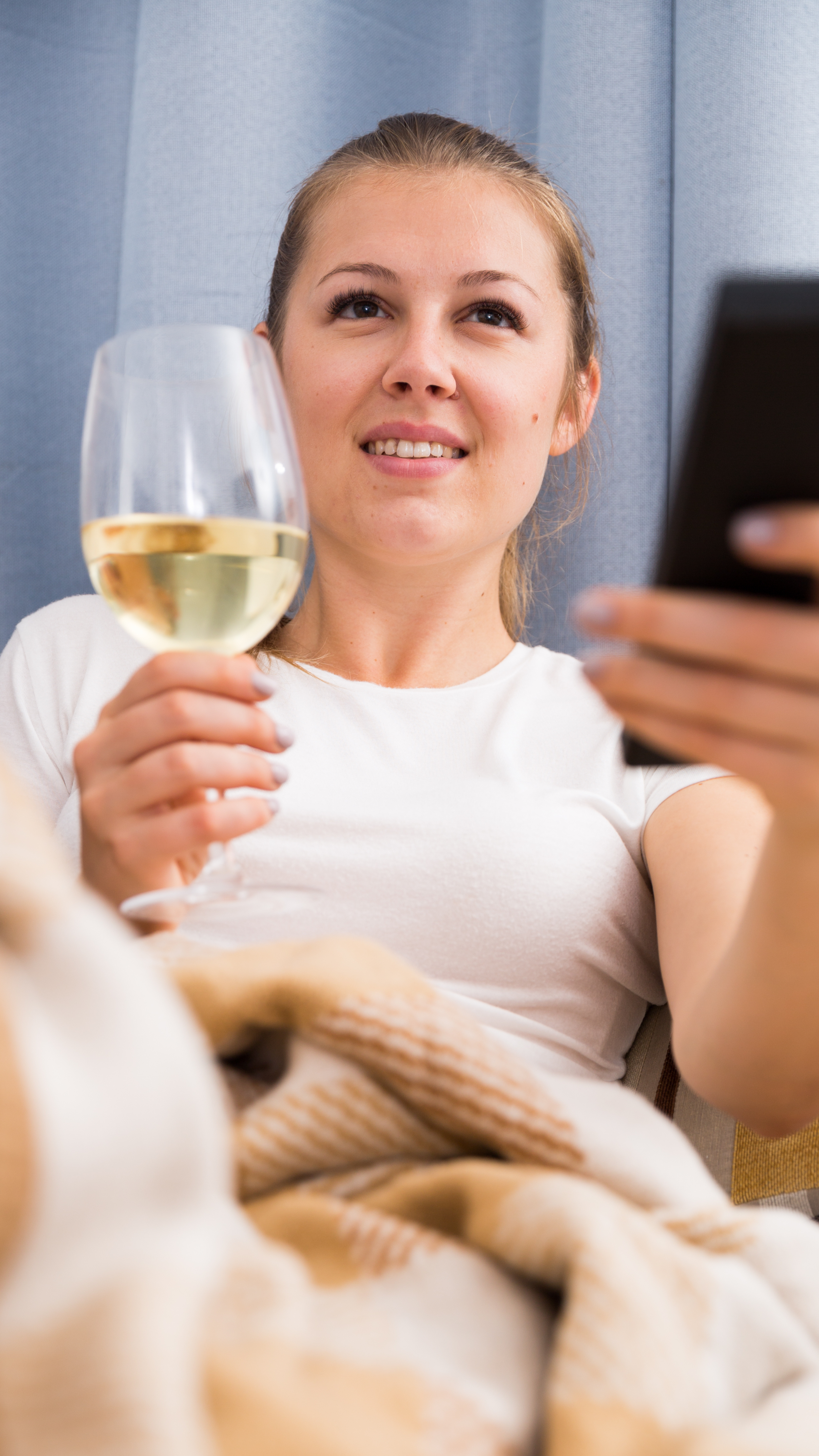 Frau hält beim Fernsehschauen ein Glas Weißwein WZG Anlass Weingenuss Serienmarathon