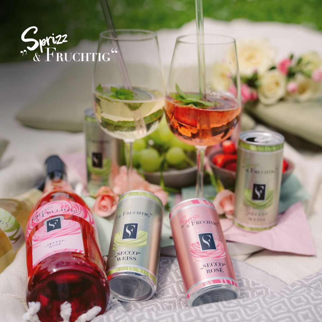 Seccoflasche und Seccodosen der Serie Sprizz und Fruchtig auf einer Picknickdecke mit zwei Weingläsern WZG Titelbild Sprizz und Fruchtig Serie